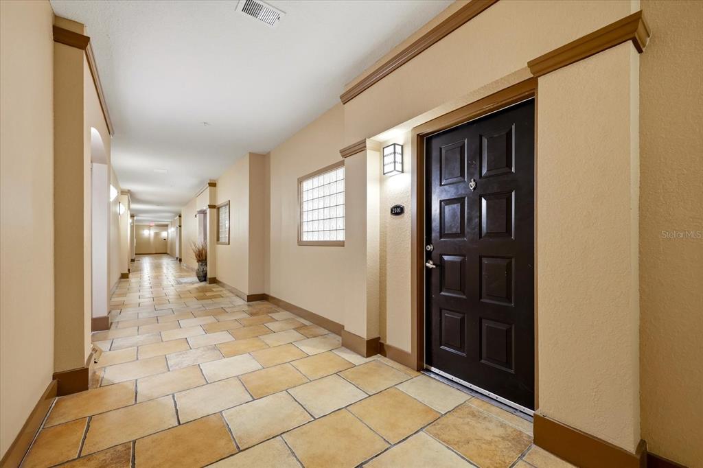 A hallway with tan tile flooring leads to a dark brown door with unit number 2101 — 4221 W SPRUCE STREET UNIT 2101, TAMPA, FL