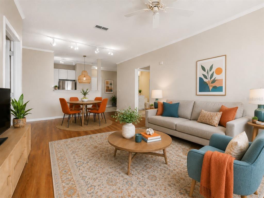 An open-concept living and dining area features wood-look flooring, a neutral sofa, and orange accents — 4221 W SPRUCE STREET UNIT 2101, TAMPA, FL