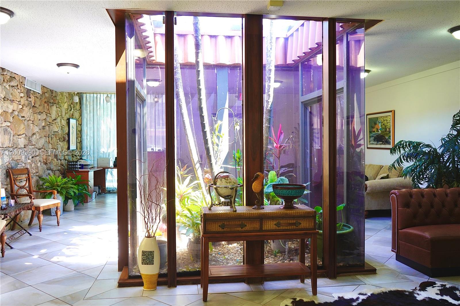 A living room features a central glass-enclosed atrium with plants and a stone accent wall — 150 Westward Dr # 4, Miami Springs FL 33166, MIAMI SPRINGS, FL
