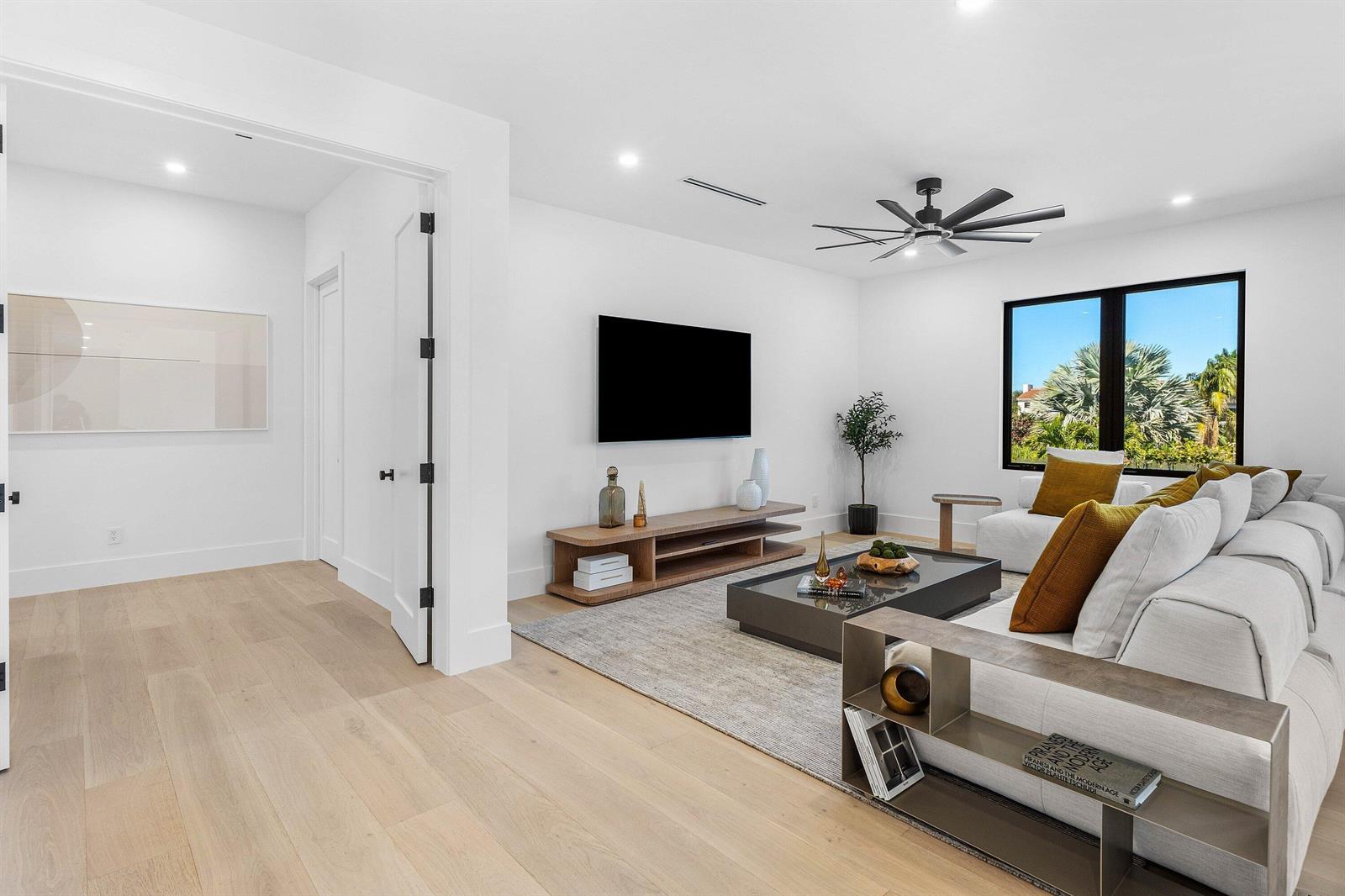 A modern living room features light wood floors, a white sectional sofa, and a television — 435 NE 15th Terrace, Boca Raton FL 33432, BOCA RATON, FL