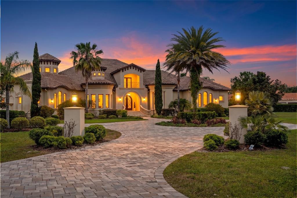 A large Mediterranean-style house with a paved circular driveway at sunset — 17301 BALLMONT PARK DRIVE, ODESSA, FL