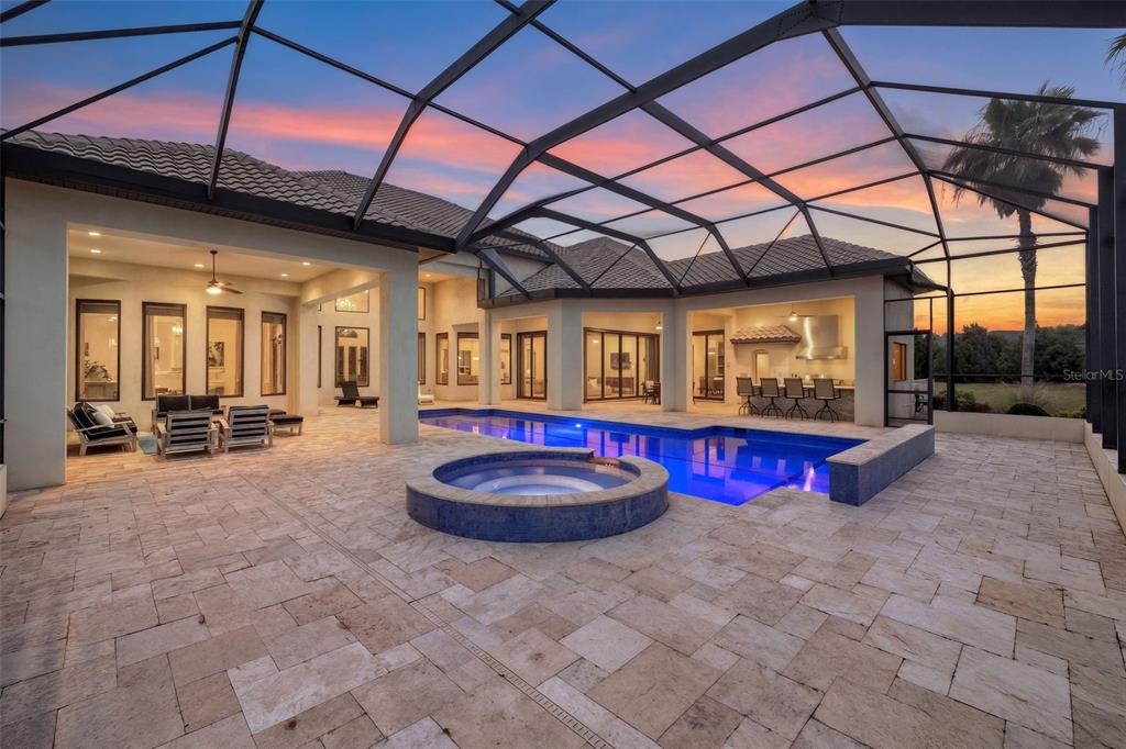 A screened-in patio features a rectangular swimming pool, a circular spa, and an outdoor kitchen — 17301 BALLMONT PARK DRIVE, ODESSA, FL