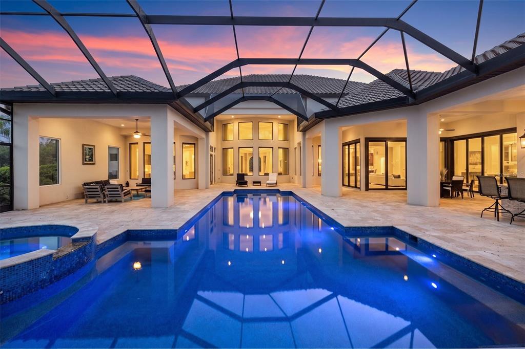 A swimming pool and hot tub sit on a stone patio inside a screened enclosure — 17301 BALLMONT PARK DRIVE, ODESSA, FL