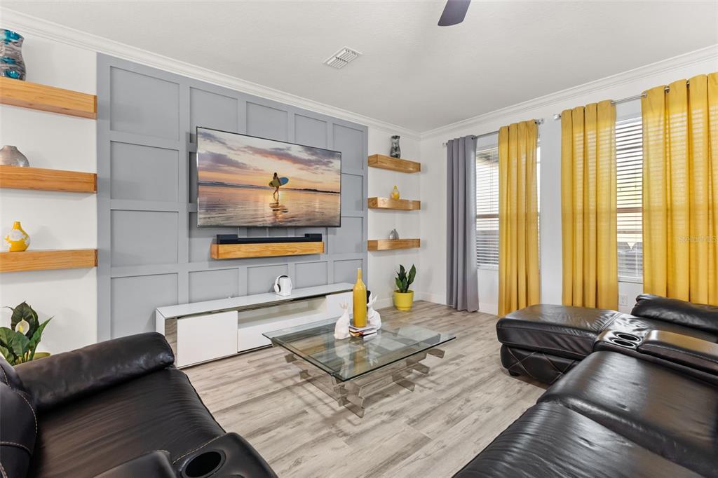 A living room features a gray paneled accent wall, floating wood shelves, and yellow curtains — 1452 SOURWOOD DRIVE, OCOEE, FL