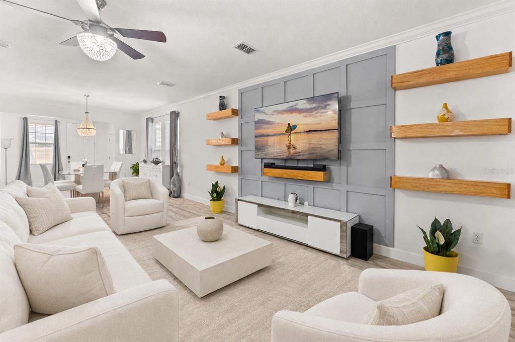 A living room features a gray paneled accent wall with a television and floating wooden shelves — 1452 SOURWOOD DRIVE, OCOEE, FL