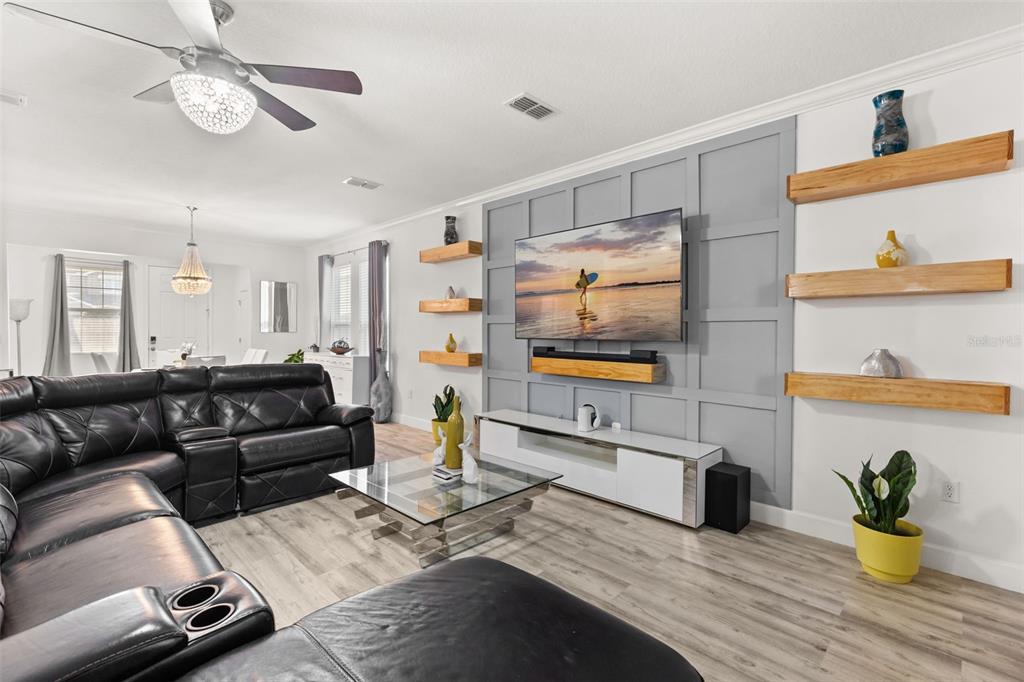 A living room features a gray paneled accent wall with a mounted television and floating shelves — 1452 SOURWOOD DRIVE, OCOEE, FL