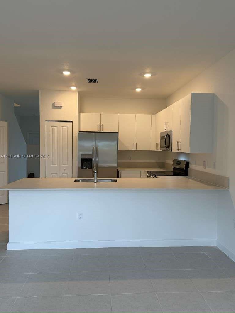 A kitchen features white cabinets, stainless steel appliances, and a peninsula with a sink — HOMESTEAD, FL