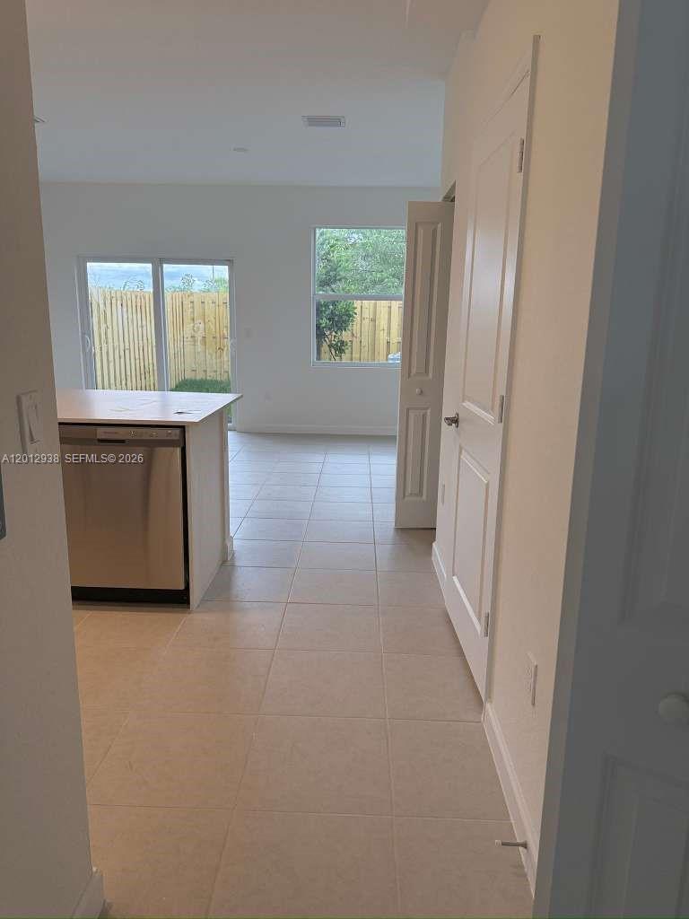 A tiled kitchen area features a stainless steel dishwasher and a view of the backyard — HOMESTEAD, FL