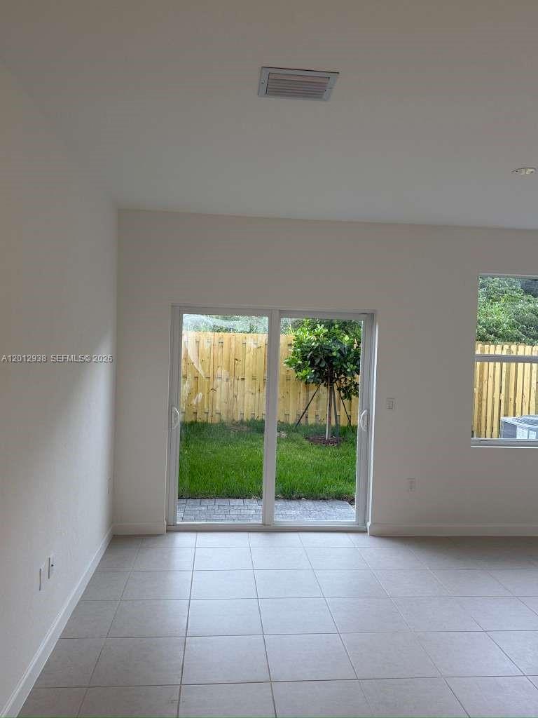 A room with light-colored tile flooring, white walls, a sliding glass door, and a window — HOMESTEAD, FL
