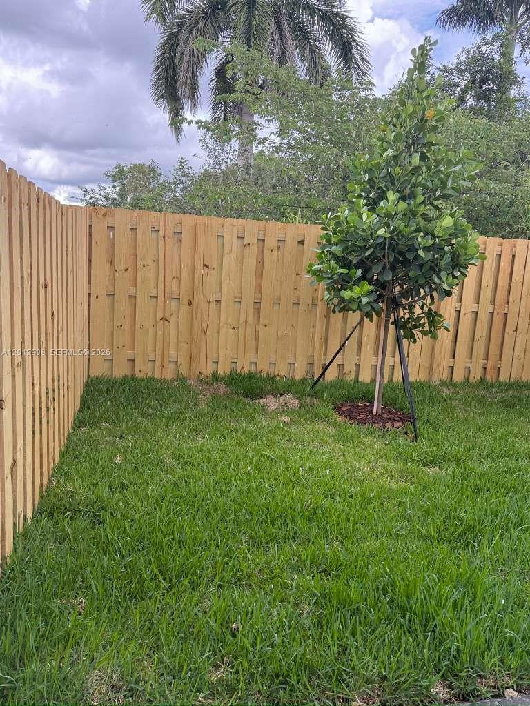 A small backyard features a green lawn, a wooden privacy fence, and a young tree — HOMESTEAD, FL