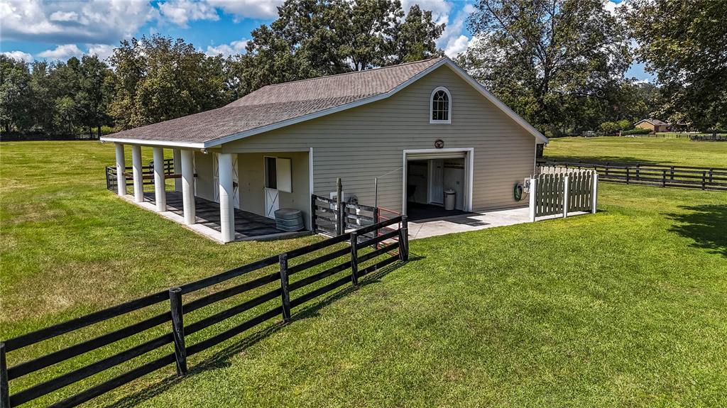 A tan barn with a covered porch and fenced pasture sits on a grassy lot — 1198 SW 104TH STREET ROAD, OCALA, FL