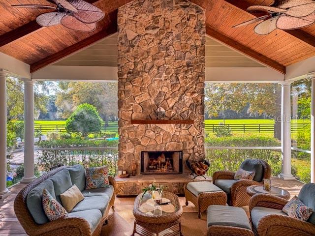 A screened-in porch features a large stone fireplace, wicker furniture, and a vaulted wood ceiling — 1198 SW 104TH STREET ROAD, OCALA, FL