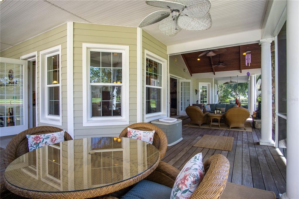 A covered wooden porch features wicker furniture, a glass-topped table, and light green siding — 1198 SW 104TH STREET ROAD, OCALA, FL