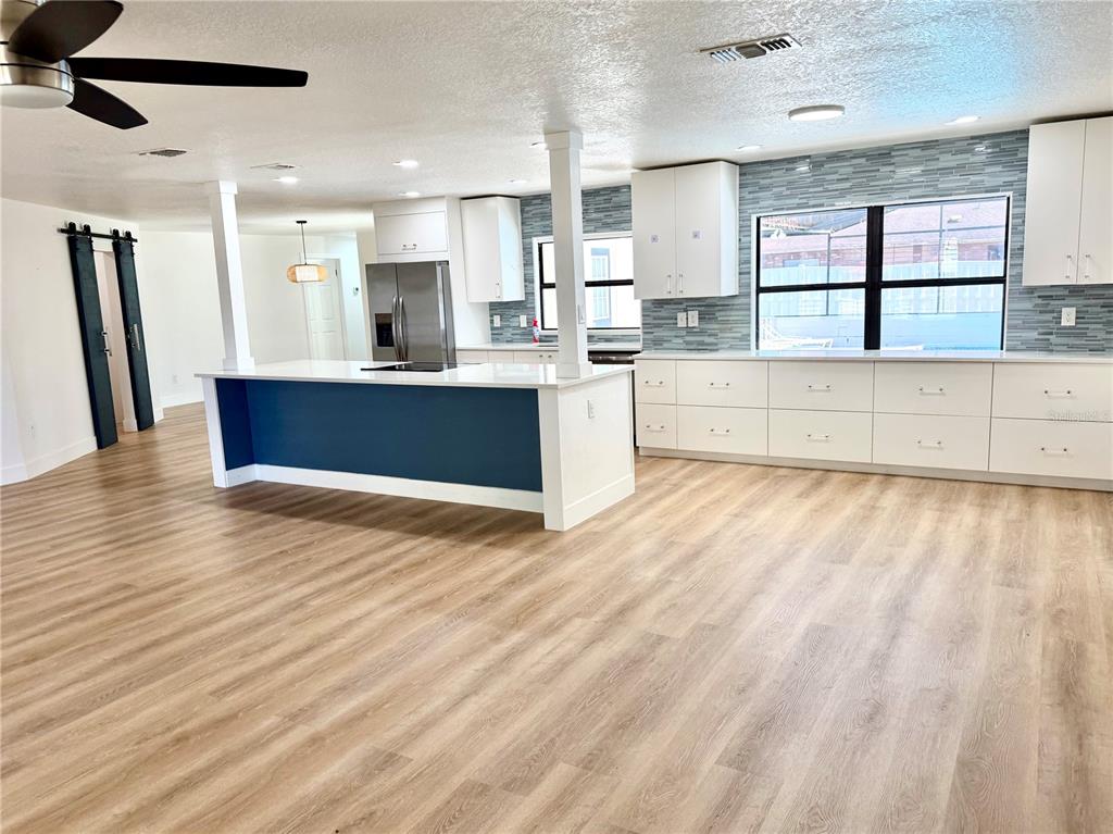 A modern kitchen features white cabinets, a blue island, and light wood-look flooring — 1325 MOLLIE ROAD, DAYTONA BEACH, FL