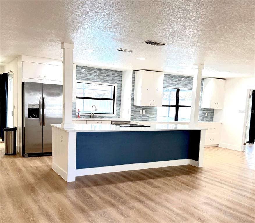 A modern kitchen features a blue island, white cabinetry, stainless steel appliances, and wood flooring — 1325 MOLLIE ROAD, DAYTONA BEACH, FL