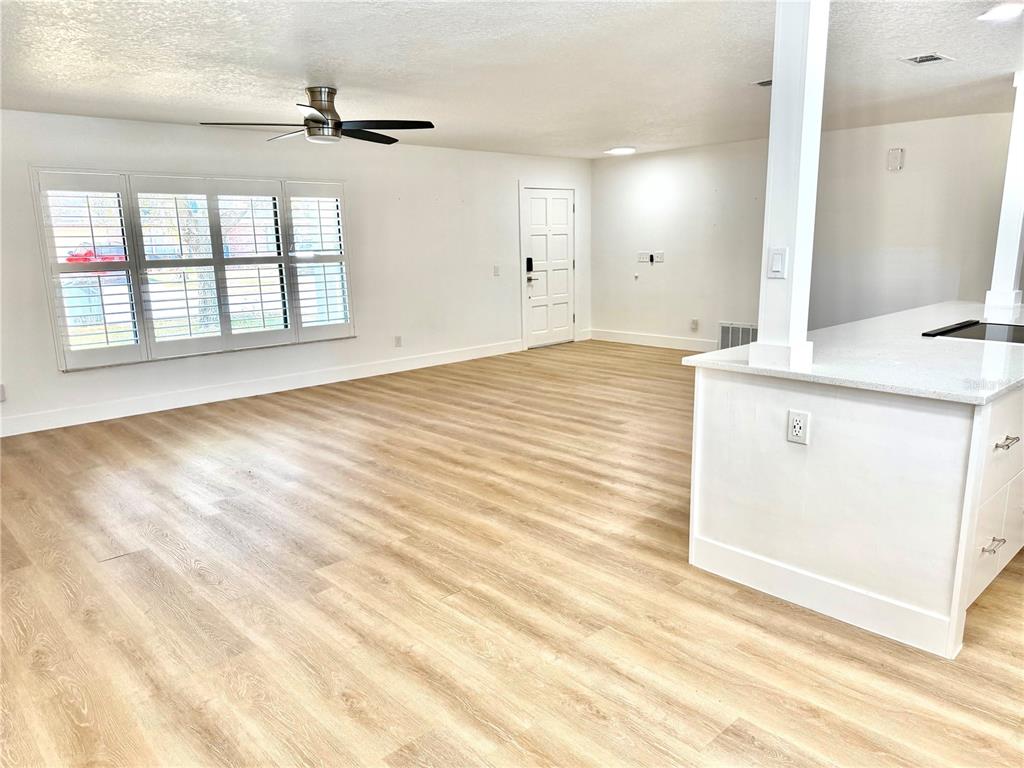 An open-concept living area features light wood-look flooring, white walls, and a kitchen island — 1325 MOLLIE ROAD, DAYTONA BEACH, FL