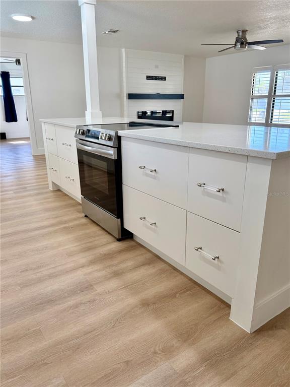 A kitchen island with a stainless steel stove and white cabinets sits on wood-look flooring — 1325 MOLLIE ROAD, DAYTONA BEACH, FL