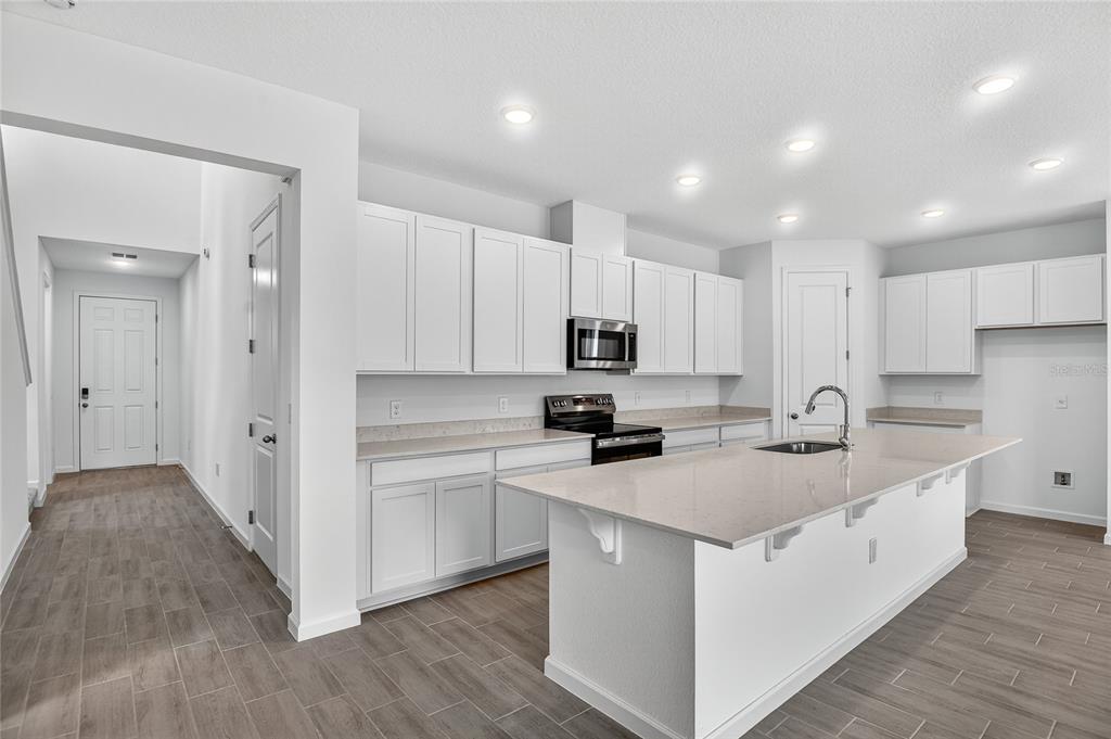 A modern kitchen features white cabinetry, quartz countertops, a center island, and wood-look tile flooring — 729 LAKE DELL AVENUE, DUNDEE, FL