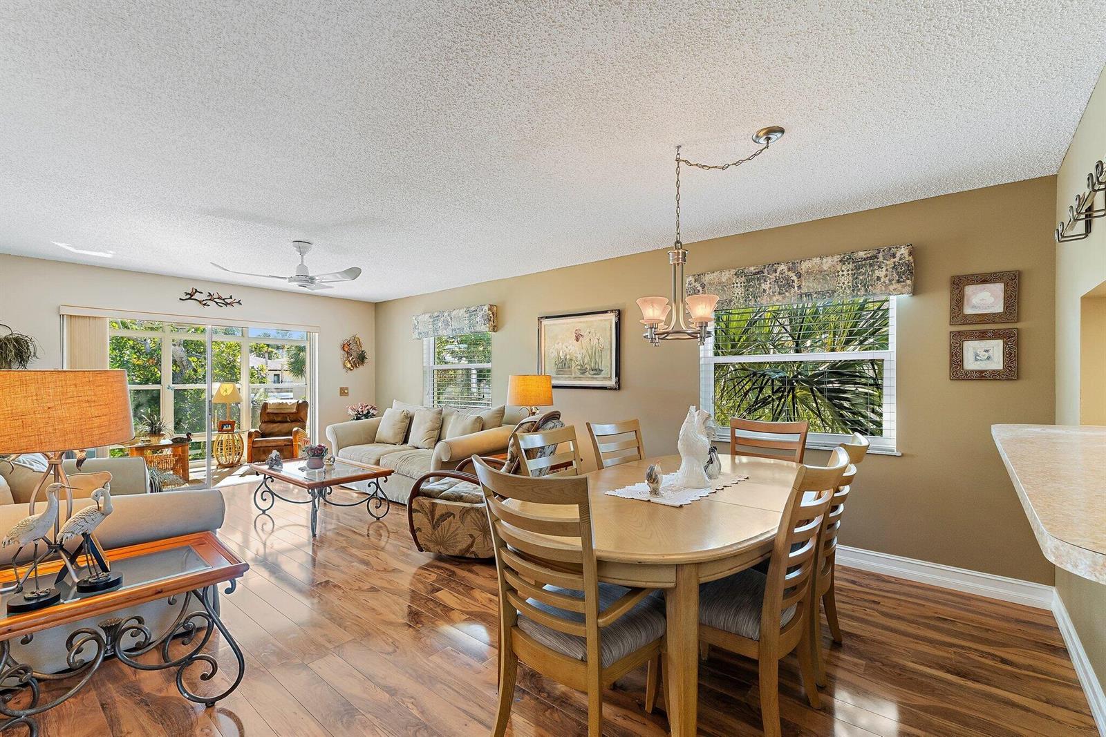 A living and dining room with wood floors, a ceiling fan, and large windows — 2950 SE Ocean Blvd. # 8, Stuart FL 34996, STUART, FL