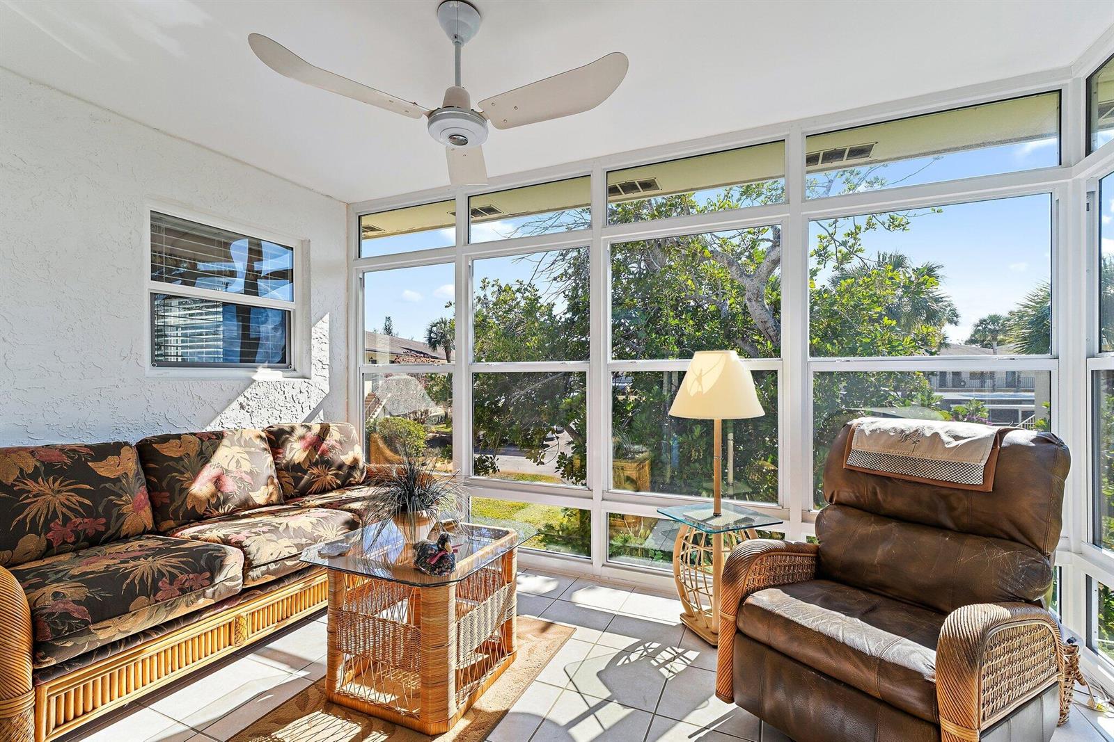 A sunroom features a floral sofa, a leather recliner, wicker furniture, and large glass windows — 2950 SE Ocean Blvd. # 8, Stuart FL 34996, STUART, FL