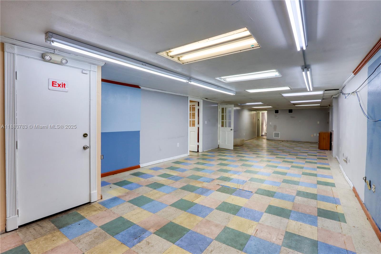 An empty room features a checkered tile floor, fluorescent ceiling lights, and multiple white doors — 6250 W 21st Ct, Hialeah FL 33016, HIALEAH, FL