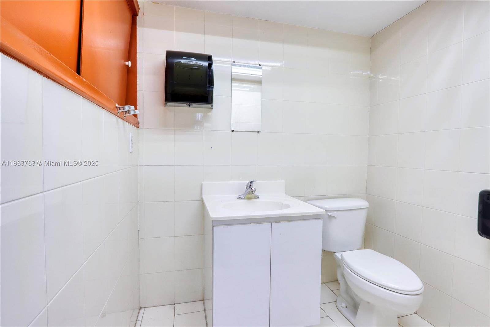 A small bathroom features white tiled walls, a vanity sink, and a white toilet — 6250 W 21st Ct, Hialeah FL 33016, HIALEAH, FL
