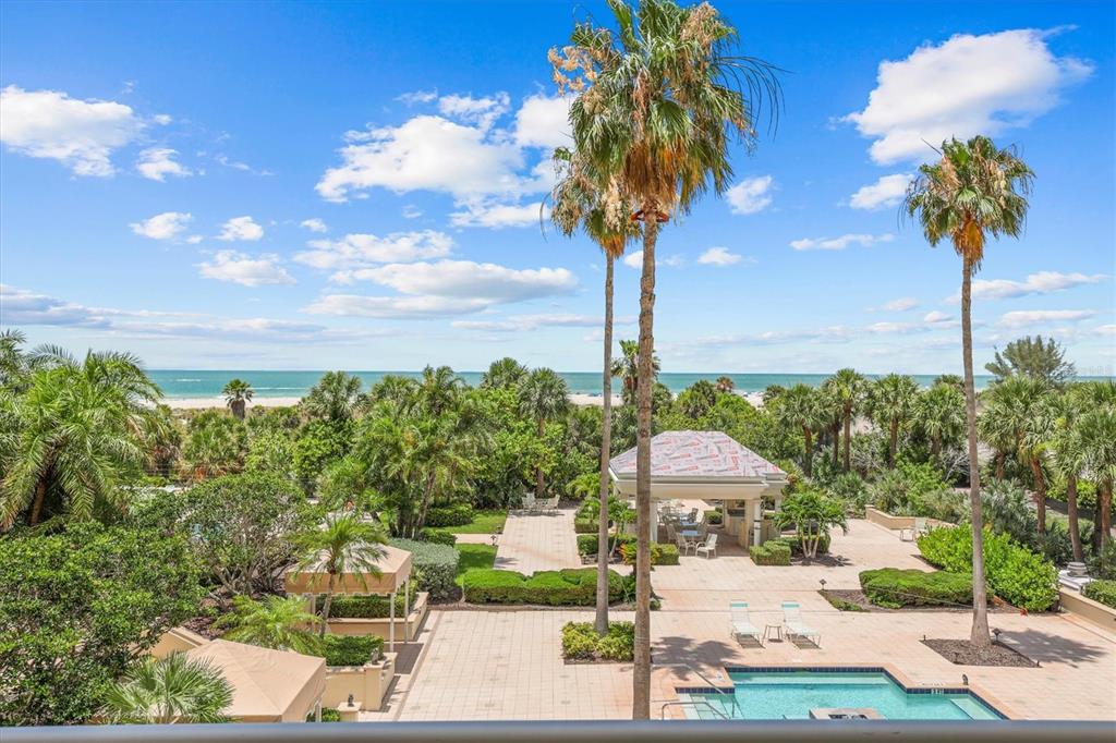 An elevated view of a swimming pool, patio, palm trees, and the ocean beyond — 1170 GULF BOULEVARD UNIT 201, CLEARWATER BEACH, FL