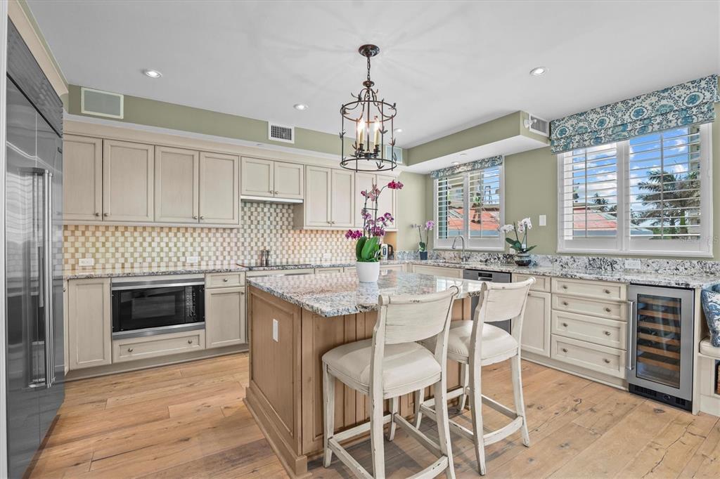 A kitchen features light wood cabinets, a granite-topped island with two chairs, and hardwood floors — 1170 GULF BOULEVARD UNIT 201, CLEARWATER BEACH, FL