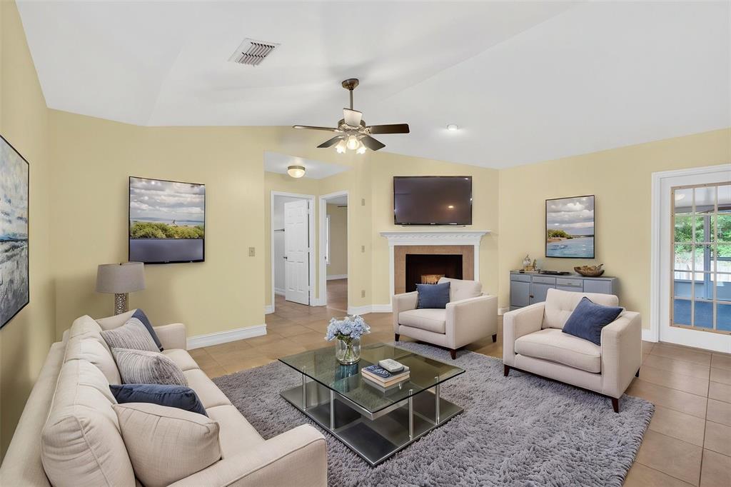 A living room features a fireplace, a glass coffee table, and beige furniture on tile — 3633 JERICHO DRIVE, CASSELBERRY, FL