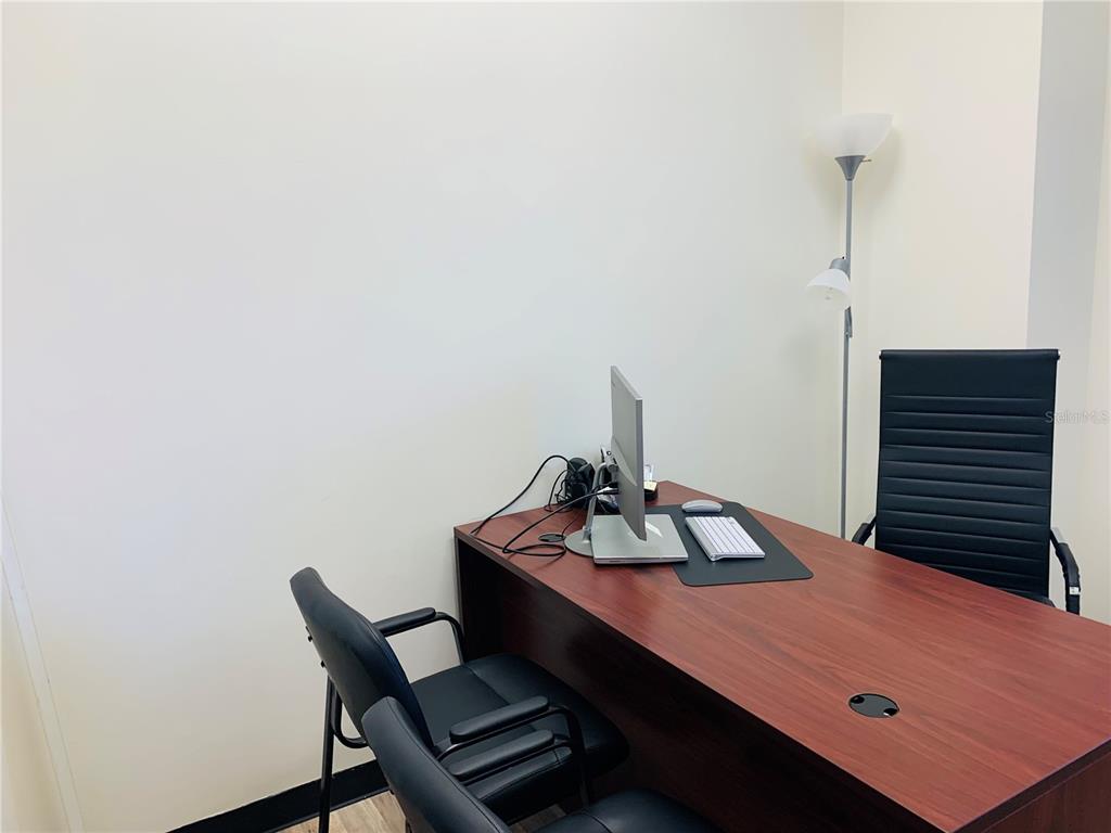 An office space features a wooden desk, two black chairs, a computer, and a floor lamp — 7065 WESTPOINTE BOULEVARD UNIT 320, ORLANDO, FL