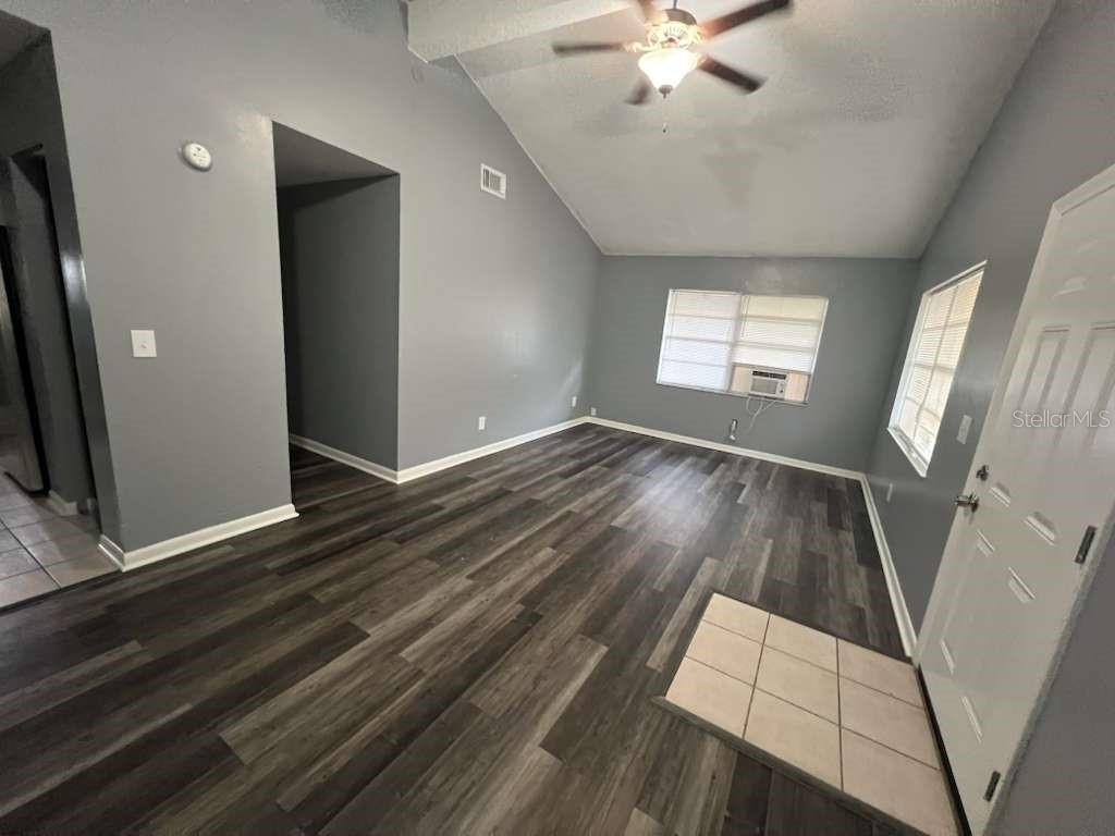 An empty living room features gray walls, vaulted ceilings, and dark wood-look laminate flooring — 8301 N ALASKA STREET, TAMPA, FL