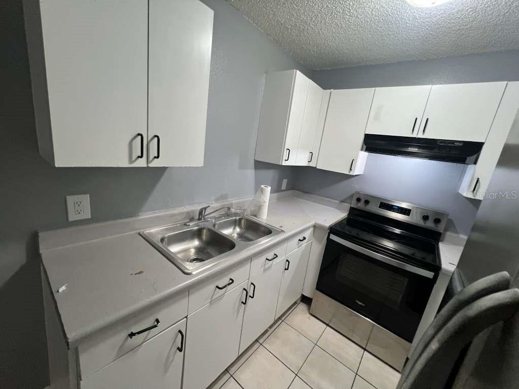 A kitchen features white cabinets, stainless steel appliances, a double sink, and tiled flooring — 8301 N ALASKA STREET, TAMPA, FL