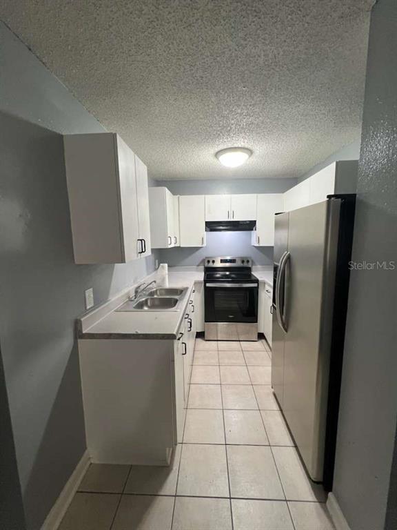 A galley kitchen features white cabinets, stainless steel appliances, and light-colored tile flooring — 8301 N ALASKA STREET, TAMPA, FL