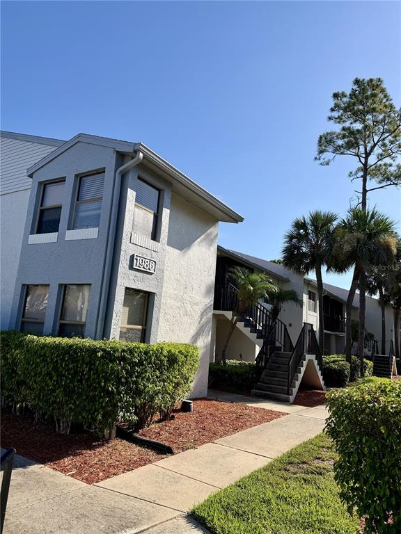 A two-story apartment building exterior with a staircase, palm trees, and a landscaped hedge — 1986 PELICAN LANDING BOULEVARD UNIT 1511, CLEARWATER, FL