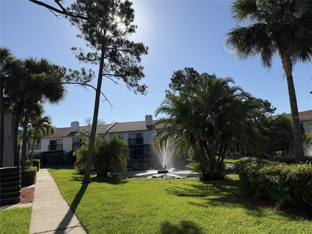 A fountain sits in a pond surrounded by palm trees and a residential apartment building — 1986 PELICAN LANDING BOULEVARD UNIT 1511, CLEARWATER, FL