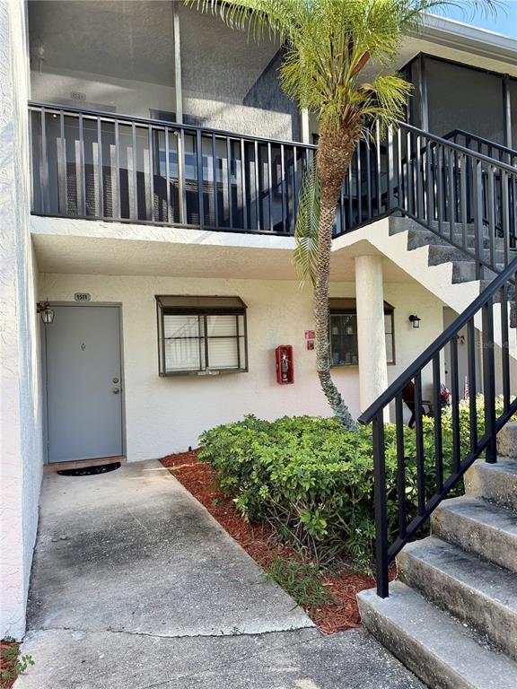 A two-story apartment building exterior features a ground-floor entrance, a staircase, and a palm tree — 1986 PELICAN LANDING BOULEVARD UNIT 1511, CLEARWATER, FL