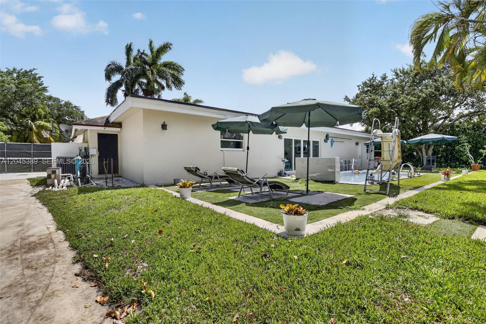 A backyard features a swimming pool, lounge chairs, umbrellas, and a slide on a lawn — 14401 SW 23rd St, Davie FL 33325, DAVIE, FL