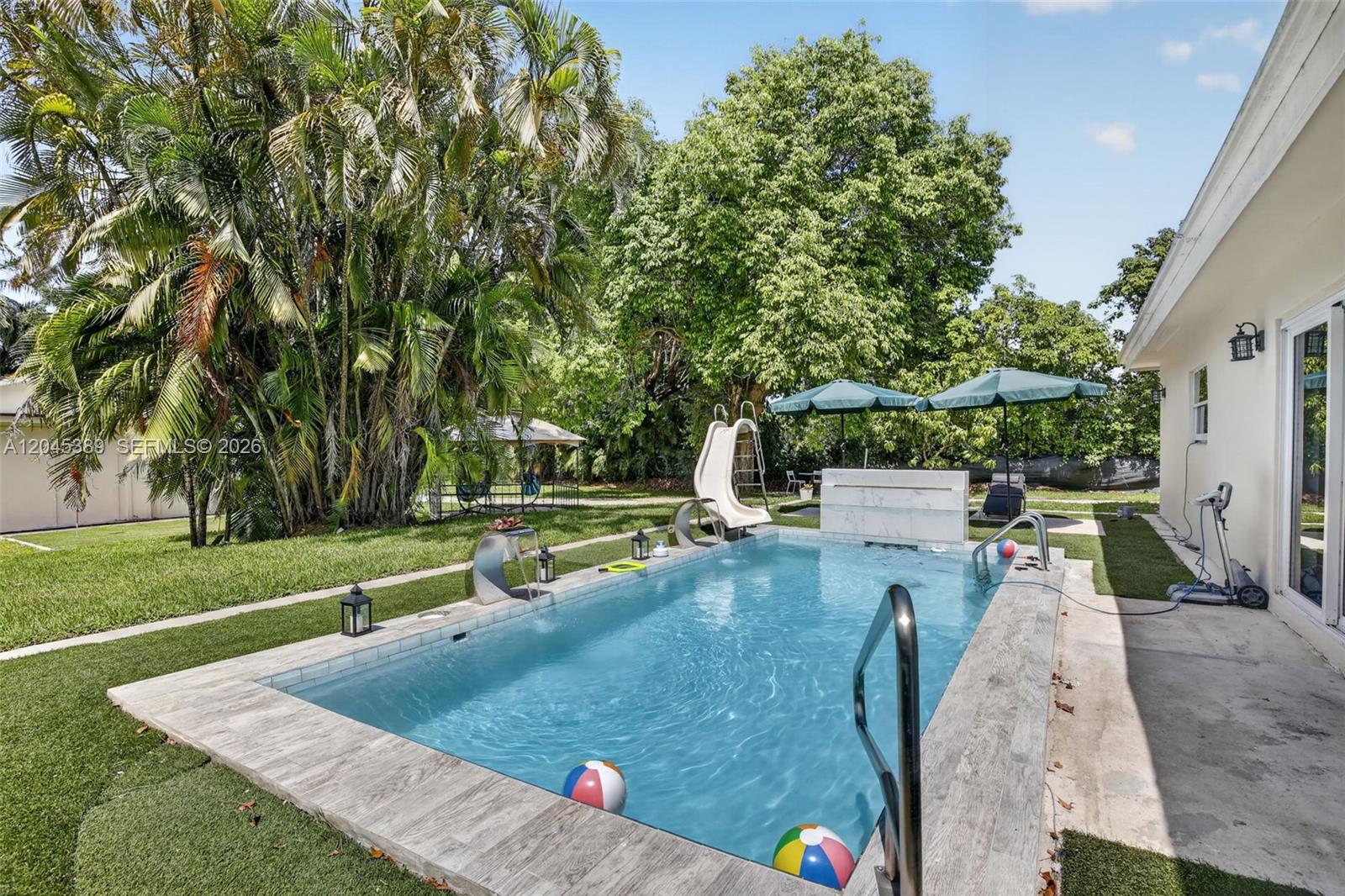 A rectangular swimming pool with a slide and water features sits in a grassy backyard — 14401 SW 23rd St, Davie FL 33325, DAVIE, FL
