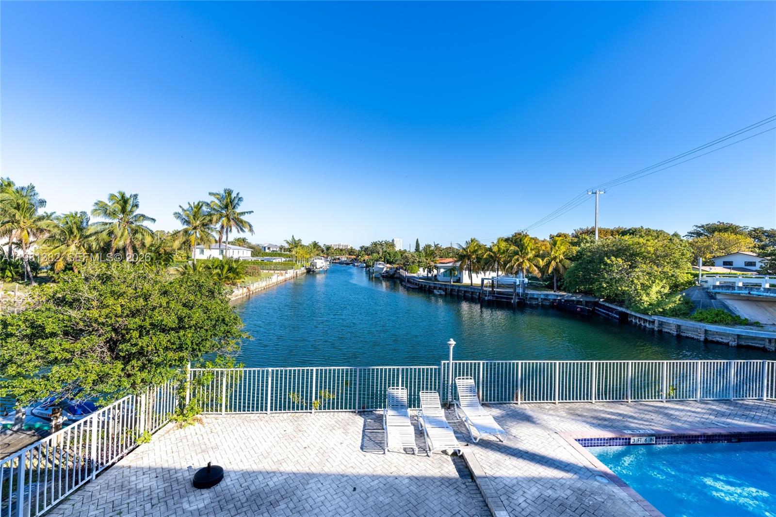 A patio with lounge chairs overlooks a canal lined with palm trees and houses — 2225 NE 123rd St # 215, North Miami FL 33181, NORTH MIAMI, FL