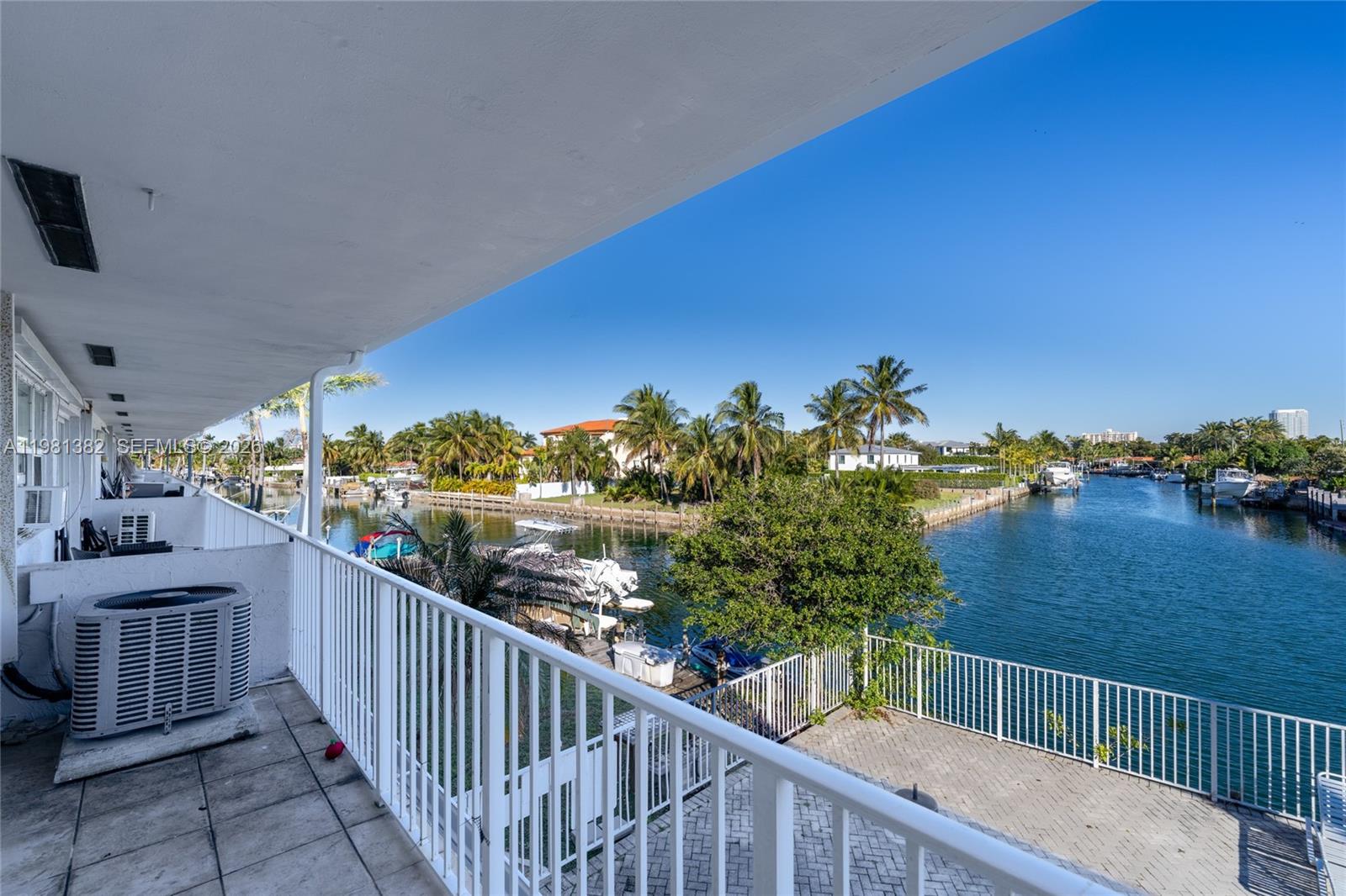 A balcony with a white railing overlooks a canal lined with palm trees and boats — 2225 NE 123rd St # 215, North Miami FL 33181, NORTH MIAMI, FL
