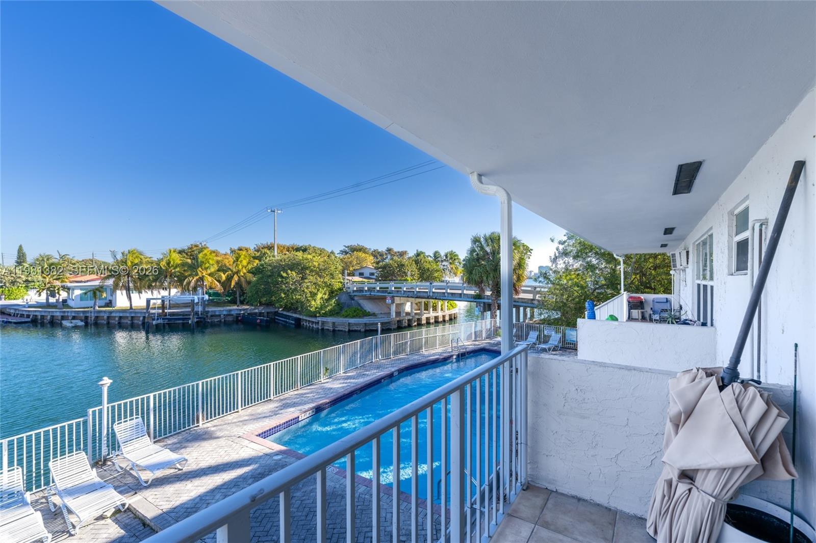 A balcony overlooks a swimming pool, a canal, and a bridge on a sunny day — 2225 NE 123rd St # 215, North Miami FL 33181, NORTH MIAMI, FL