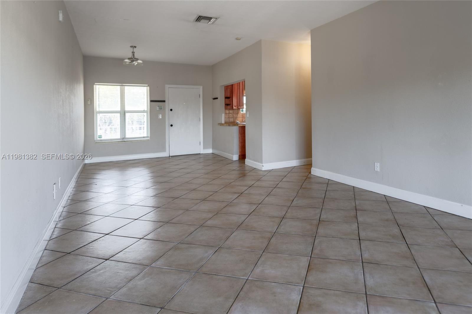 An empty living room features diagonal floor tiles, light gray walls, and a kitchen pass-through — 2225 NE 123rd St # 215, North Miami FL 33181, NORTH MIAMI, FL