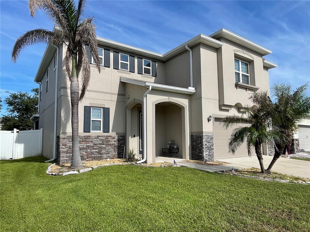 A two-story suburban house features a tan stucco exterior, stone veneer accents, and palm trees — 4501 BALER TRAILS DRIVE, ST CLOUD, FL