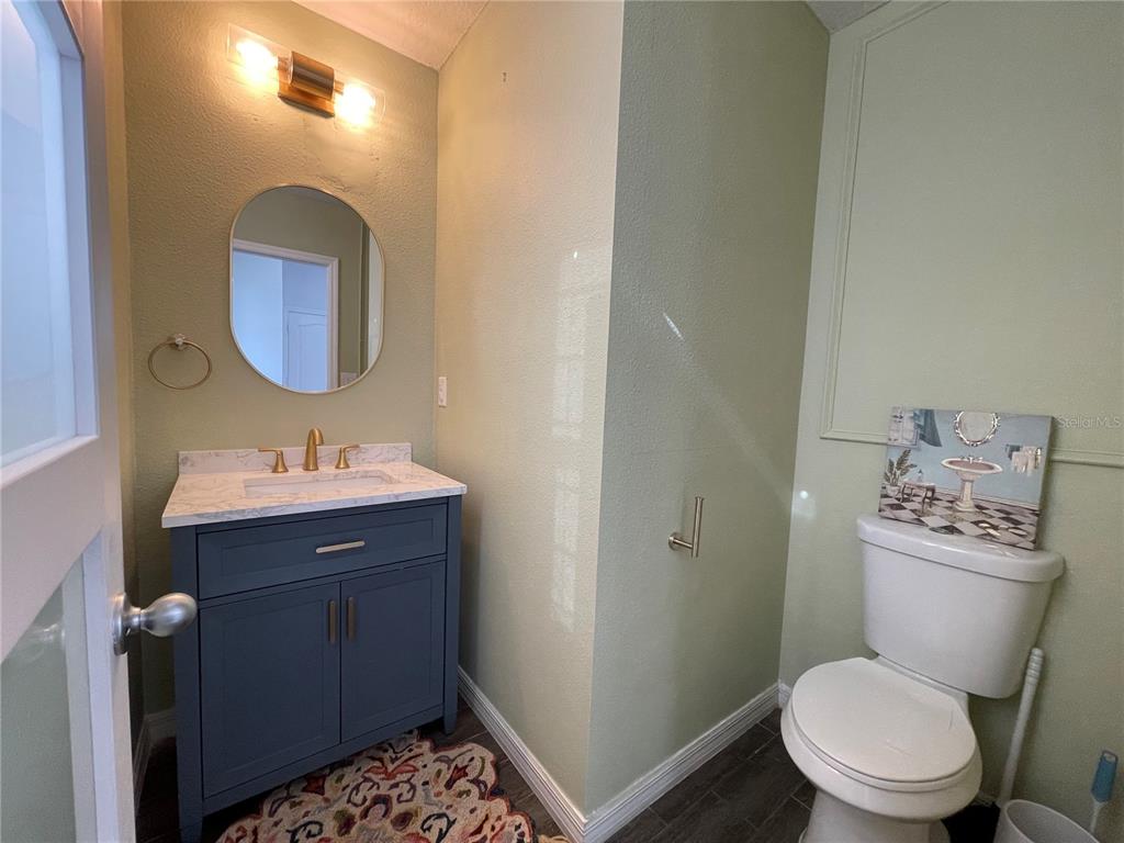 A small bathroom features a blue vanity, marble-look countertop, round mirror, and a white toilet — 4501 BALER TRAILS DRIVE, ST CLOUD, FL