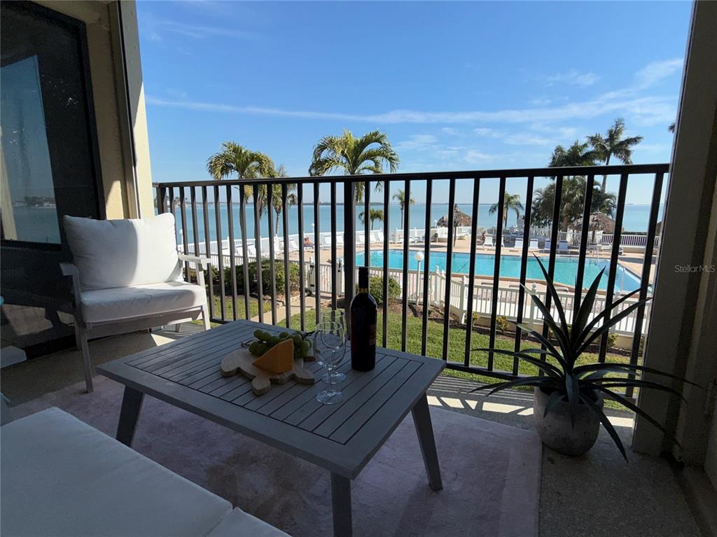 A balcony features a table with wine and snacks, overlooking a swimming pool and ocean — 6322 PALMA DEL MAR BOULEVARD S UNIT 213, ST PETERSBURG, FL