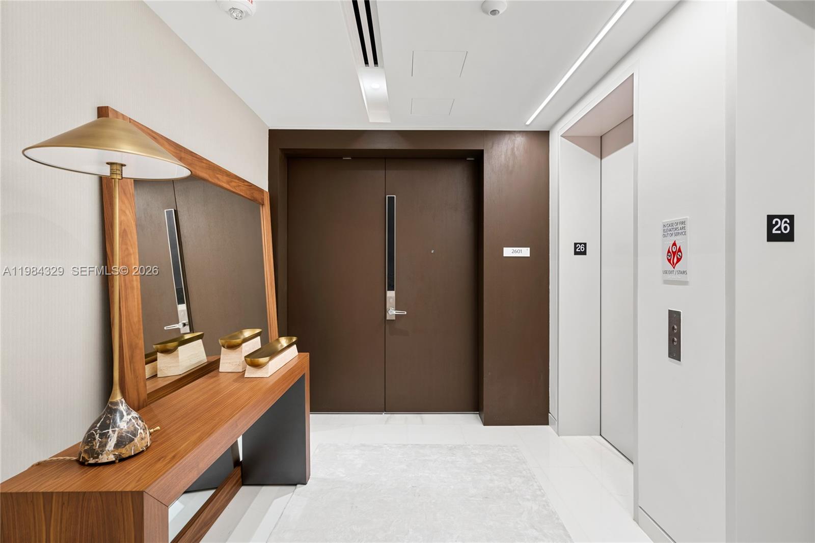 A modern apartment entryway features a wooden console table, a mirror, and an elevator door — 300 Biscayne Boulevard Way # 2601E, Miami FL 33131, MIAMI, FL