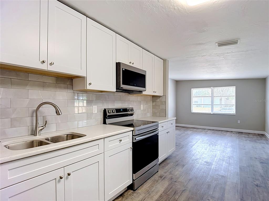 A kitchen with white cabinets, stainless steel appliances, and light wood-look flooring — 7133 ABIGAIL DRIVE, PORT RICHEY, FL