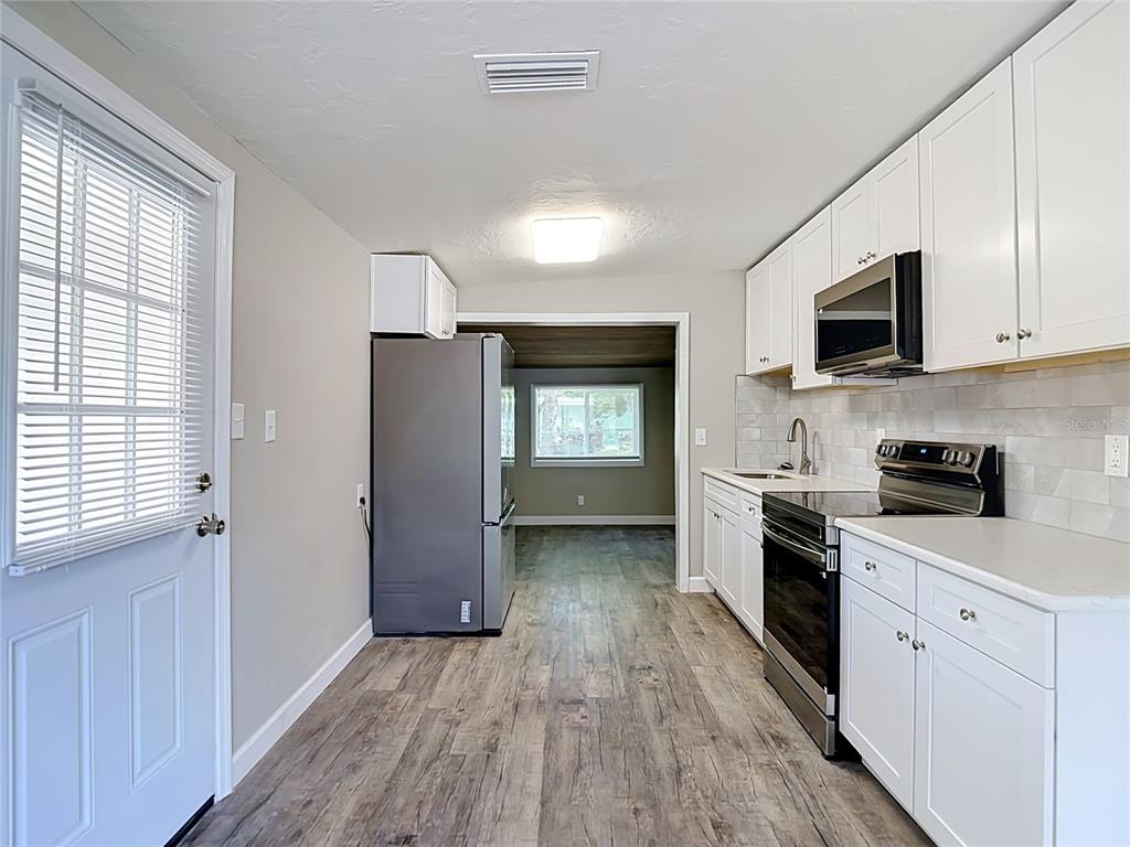 A kitchen features white cabinets, stainless steel appliances, and wood-look flooring — 7133 ABIGAIL DRIVE, PORT RICHEY, FL
