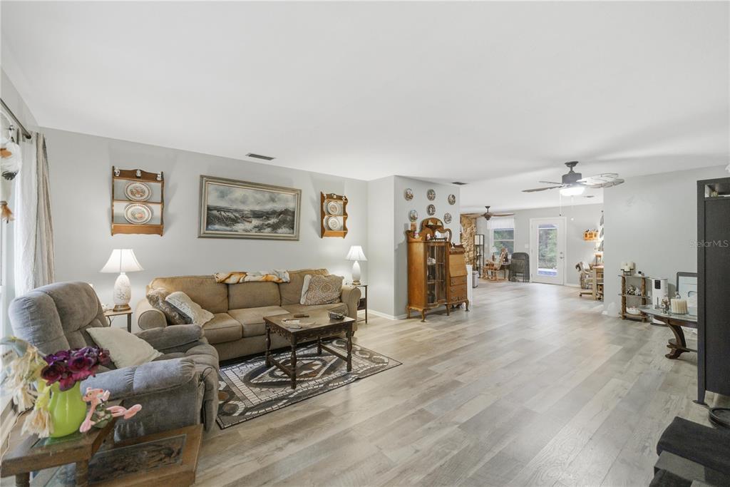 A living room features light wood-look flooring, a beige sofa, and a gray recliner — 8951 SW 202ND AVENUE ROAD, DUNNELLON, FL