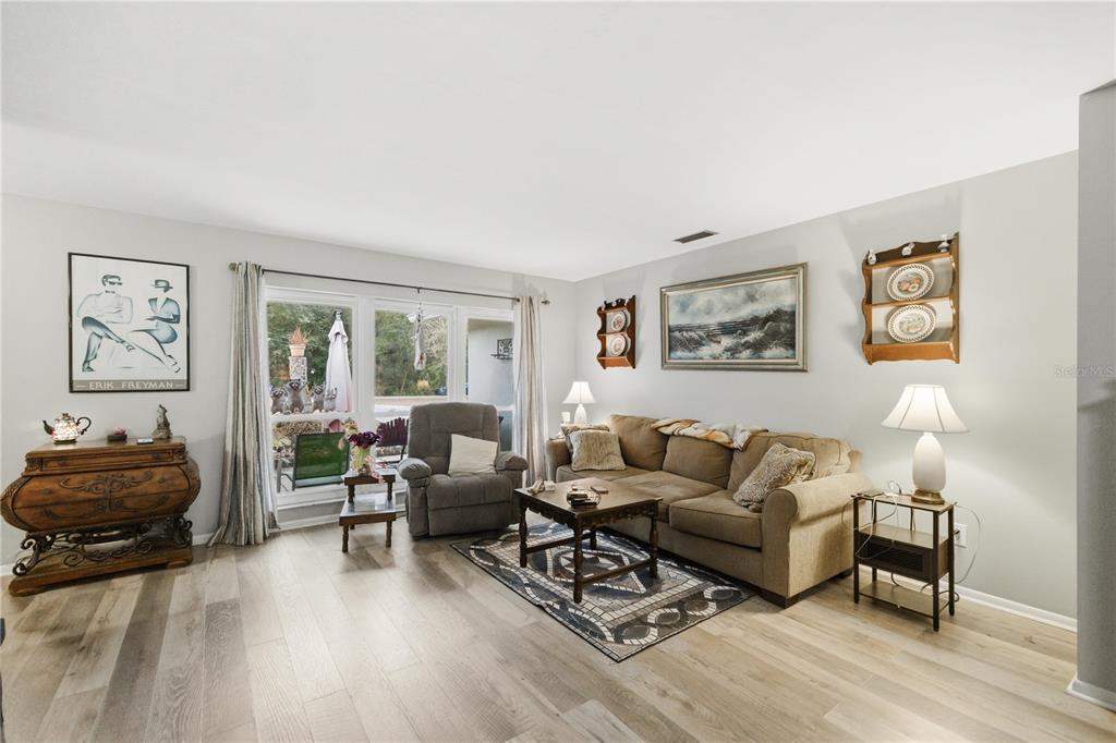 A living room features light wood-look flooring, a beige sofa, and a large window — 8951 SW 202ND AVENUE ROAD, DUNNELLON, FL
